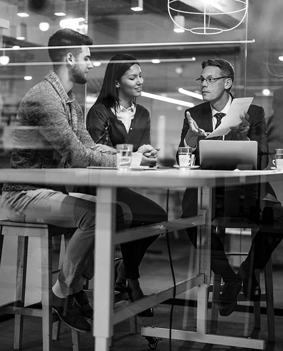 Young couple going through paperwork with their insurance agent during a meeting in the office. The view is through glass.